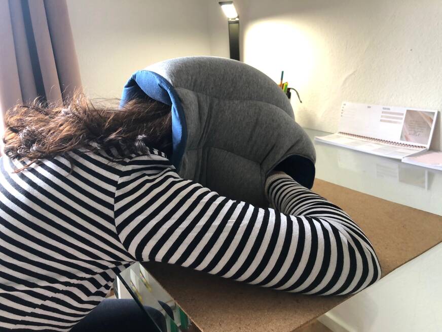 frau sitzt mit dem kopf auf dem tisch liegend mit dem ostrich pillow